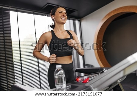 Happy young caucasian woman in good mood on treadmill. Brunette wears sports top and leggings. Strength exercise concept Royalty-Free Stock Photo #2173151077