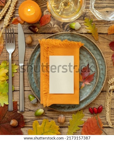 Autumn rustic table setting with blank place card and envelope between colorful leaves and berries, top view, mockup. Flat lay Horizontal card on wooden table, copy space. Thanksgiving or harvest 