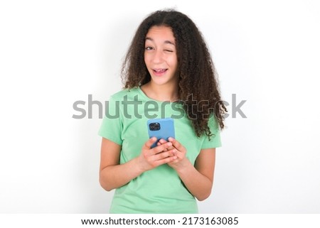 Teenager girl with afro hair style wearing green t-shirt over white background taking a selfie  celebrating success