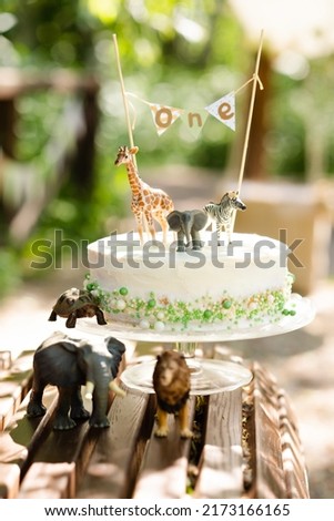 Minimalism birthday cake in scandinavian style for baby for first year birthday. On natural background, with animal toys decor. Photo zone for toddler. Eco birthday party.