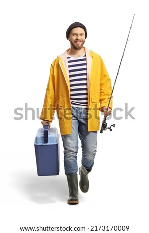 Full length portrait of a young fisherman holding a fishing rod and fridge and walking towards camera isolated on white background Royalty-Free Stock Photo #2173170009