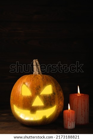 Halloween pumpkin on brown wood texture with candles. Composition on a dark background. Scary composition with glowing eyes and mouth. Holiday concept. copy space