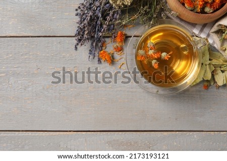 Freshly brewed tea and dried herbs on grey wooden table, flat lay. Space for text