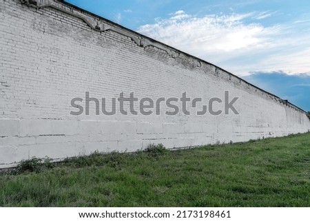 Long spacious empty old white colored brick wall structured on green grass against blue sky