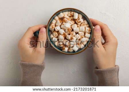 Cup of tasty cocoa drink and marshmallows in hands.Spices and marshmallows for winter drinks on a textured background.Winter hot drink.Hot chocolate with marshmallow and spices.Copy space.