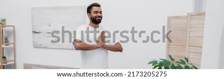 happy african american man african american man meditating with praying hands near folding screen, banner