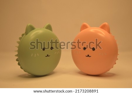 two round fan objects of green and pink in the shape of a cat's head are facing each other.