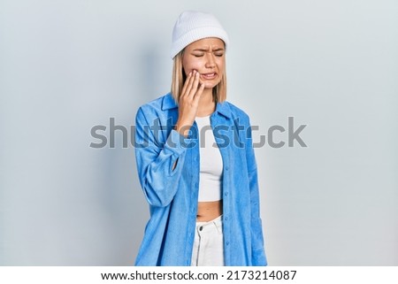 Beautiful blonde woman wearing wool hat touching mouth with hand with painful expression because of toothache or dental illness on teeth. dentist 
