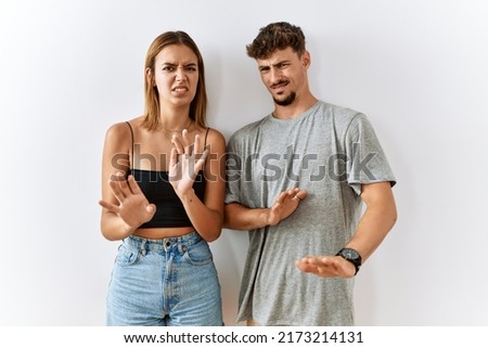 Young beautiful couple standing together over isolated background disgusted expression, displeased and fearful doing disgust face because aversion reaction.  Royalty-Free Stock Photo #2173214131