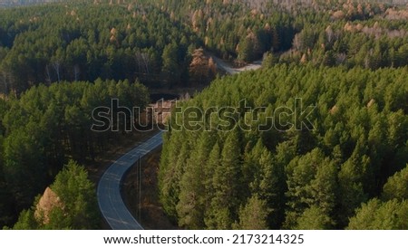 Closeup road between yellow and green autumn forest in Ural, Russia. Beautiful autumn nature landscape at during daytime. Aerial view from a drone