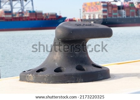 Sturdy metal mooring bollard at pier big black installed on concrete with a rope attached.  Used for large cargo berth use ropes to keep ships from moving. Single mooring device. blur background.