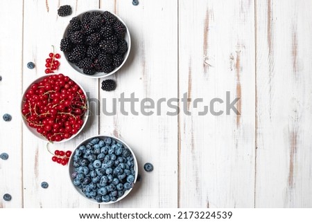 Fresh assorted berries - blueberries, blackberries and red currants in a plate on a white wooden background. Place for your text.
