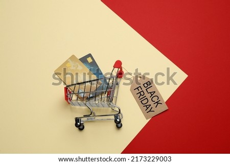 Shopping cart, credit cards and tag with phrase BLACK FRIDAY on color background, flat lay