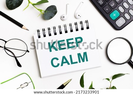On a white background there are business accessories - a calculator, a pen, glasses, a magnifying glass, a computer mouse and a notebook with the text KEEP CALM. Office desk close-up. Flat lay.