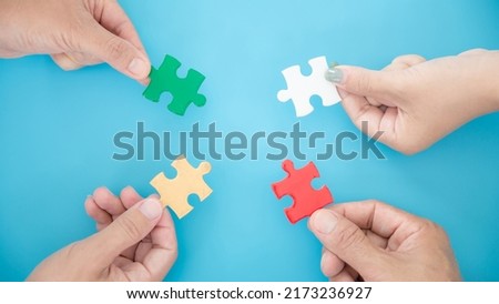 High Angle View Of Businesspeople Hand Solving Jigsaw Puzzle On Blue Background