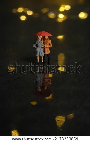 Miniature people toy figure photography. Couple dating at rainy day using umbrella at night. Beautiful golden yellow bokeh city light background. Image photo