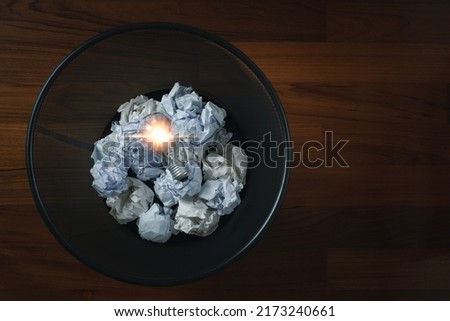 Top view of crumpled paper with light bulb in garbage bin. Concept creative idea in trash.