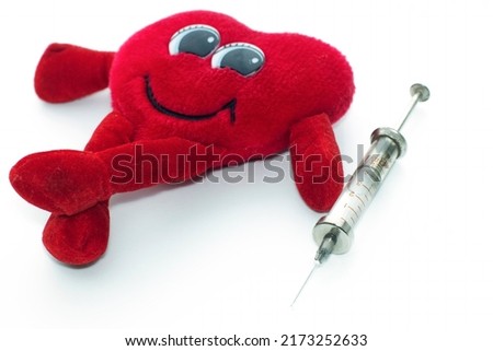a cheerful toy heart, lies cross-legged, next to a medical syringe, on an isolated white background