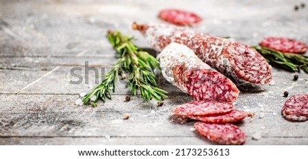 Pieces of salami sausage with sprigs of rosemary. On a gray background. High quality photo