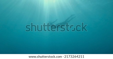 Woman silhouette floating underwater in beautiful blue sea with sun rays. Freediving diving on a breath hold. Unfocused image Royalty-Free Stock Photo #2173264211