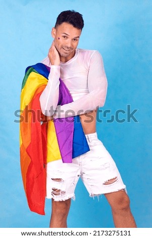 gay guy smiling with the pride flag over his shoulder, blue background . High quality photo