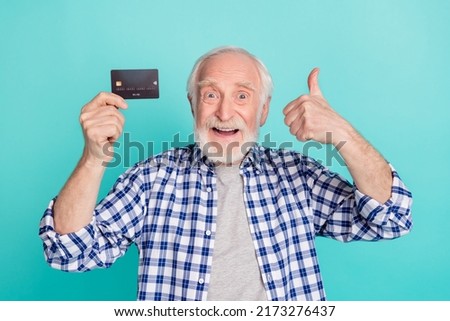 Photo of funny granddad hold show debit card thumb up isolated on turquoise color background