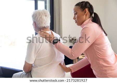 Biracial female physiotherapist giving back massage therapy to caucasian senior man at home. Physiotherapy and rehabilitation concept Royalty-Free Stock Photo #2173281927