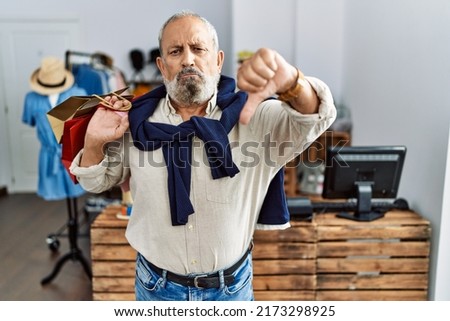 Handsome senior man holding shopping bags at boutique shop looking unhappy and angry showing rejection and negative with thumbs down gesture. bad expression.  Royalty-Free Stock Photo #2173298925