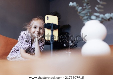 Cute little caucasian girl with blonde hair in trendy casual clothes using mobile phone in modern cafe at spring. Video chat and social distancing during coronavirus covid-19 pandemic lockdown
