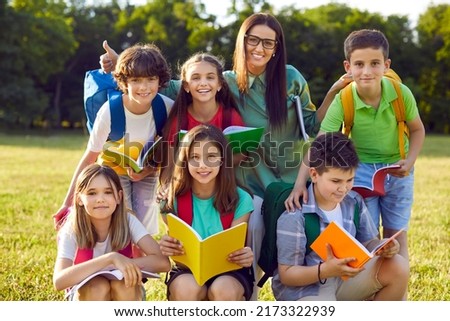 Outdoor portrait of happy modern Caucasian school children together with their teacher. Beautiful young woman and her elementary students posing for group photo in the park during fun lesson outside Royalty-Free Stock Photo #2173322939