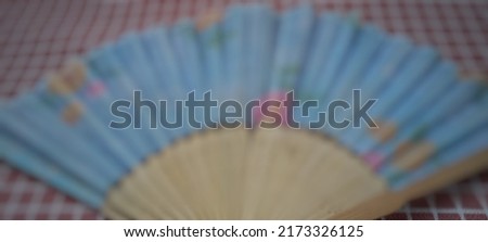 Defocused abstract background of the folding hand fan is a functional item and a stylish addition that is easy to carry on the go, can be made from a variety of materials, such as silk and hemp Royalty-Free Stock Photo #2173326125