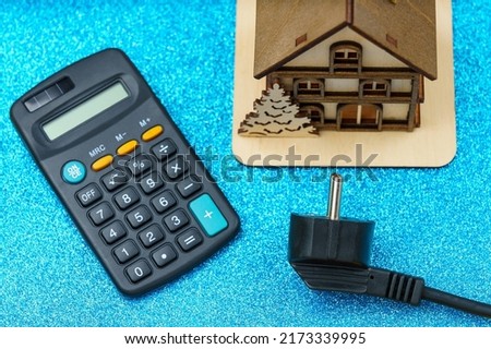 Plug from an extension cord on a blurred background of a calculator and symbolic house, selective focus. The concept of the energy crisis and electricity inflation. Rising electricity prices