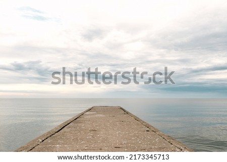 Empty concrete pier to the sea with dramatic sky and calm water, abandoned industrial jetty  Royalty-Free Stock Photo #2173345713