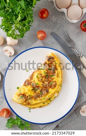 Omelet with fried mushrooms and fresh herbs in a plate on a concrete background. Delicious healthy breakfast. Top view. Copy space Royalty-Free Stock Photo #2173347029