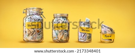 Four glass jars for savings, cash money (dollar banknotes) on yellow background. For utility bills: heating, electricity, water. Savings for life and food