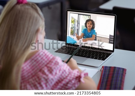 Caucasian girl with blond hair writing while studying online through video call over laptop at home. Unaltered, childhood, wireless technology, education, student and e-learning concept.