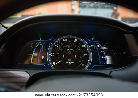 Car counter showing power monitor of engine and battery use in a hybrid vehicle. Panel with illuminated display indicating battery charge, energy level, speedometer, tachometer, odometer, fuel gauge.