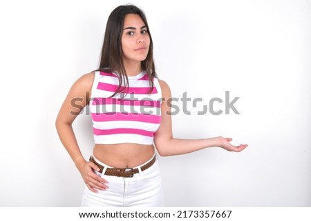 Portrait of Young beautiful brunette woman wearing striped crop top  with arm out in a welcoming gesture.