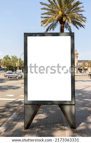 Blank vertical street billboard with palm trees and cityscape on a sunny day.