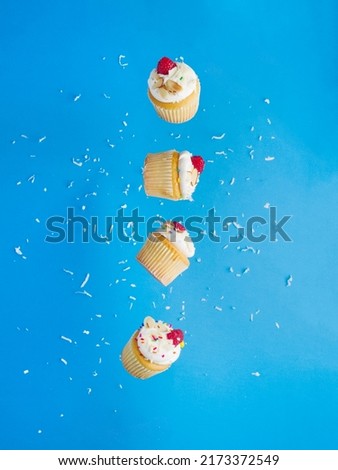 Cupcakes with cream and raspberries in free flight on a blue background. Festive creative composition. Minimalism. There are no people in the photo. There is free space to insert.