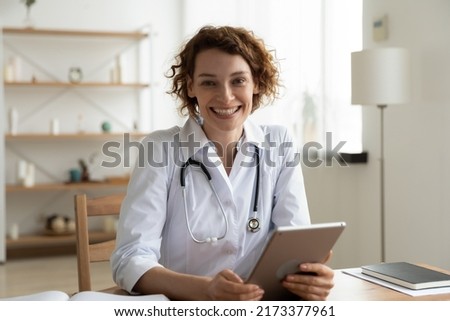 Head shot portrait smiling woman doctor holding digital tablet looking at camera, friendly young nurse physician gp working online, consulting patient, browsing medical apps, sitting at desk Royalty-Free Stock Photo #2173377961