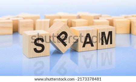 four wooden blocks with the letters SPAM - on the bright surface of a blue table. the inscription on the cubes is reflected from the surface.