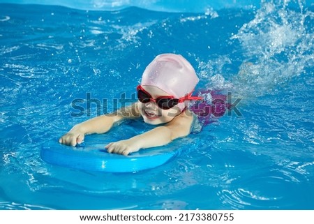 Little girl learning to swim in indoor pool with pool board