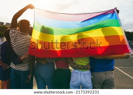 Young diverse people having fun holding lgbt rainbow flag outdoor - Main focus on african guy back Royalty-Free Stock Photo #2173392231