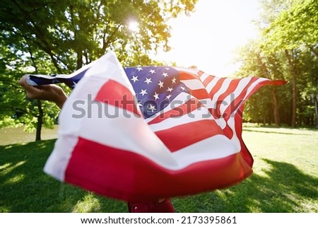 Young African american woman is waving American flag on top of at nature background. USA resident, US citizen. Immigration concept                               