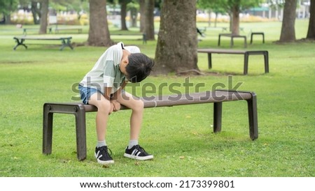 An elementary school boy who is depressed and sits on a park bench Royalty-Free Stock Photo #2173399801