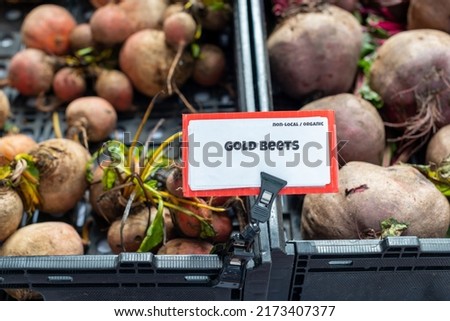 A bunch of round bright red and purple color organic gold beets in a black plastic container for sale at a farmers market.  There's a white and red sign with gold beets in black lettering on the sign.