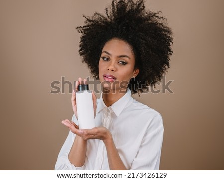 Beauty Latin woman with afro hairstyle. Brazilian woman. Holding blank shampoo packaging. Curly hair. Hair style. Pastel background.