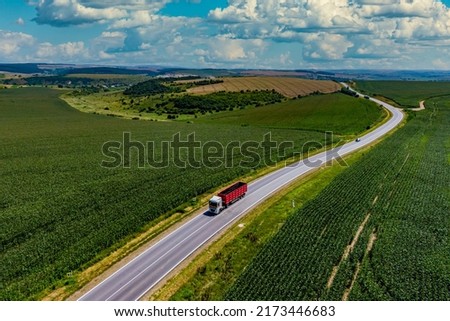 red truck driving on asphalt road along the green fields. Aerial view landscape. drone photography. cargo delivery and transportation concept 