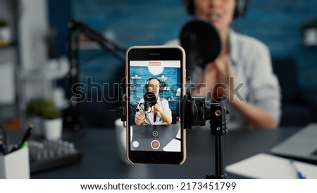 Modern smartphone recording vlogger talking to public while sitting at home studio desk. Famous influencer filming podcast show with touchscreen display device while sitting in living room. Close up